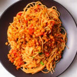 Green lentil bolognese and spaghetti in a black plate.