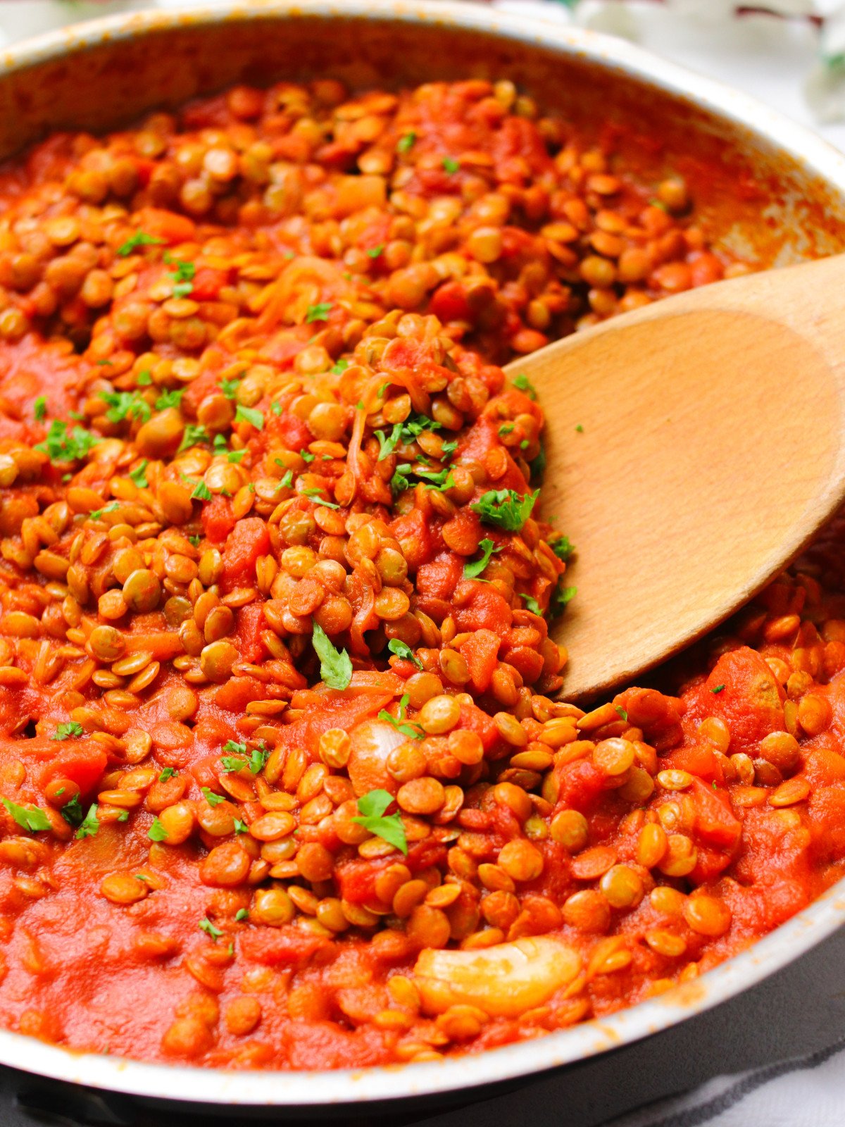Lentil bolognese with parsley on top, a wooden spoon in a silver pan.