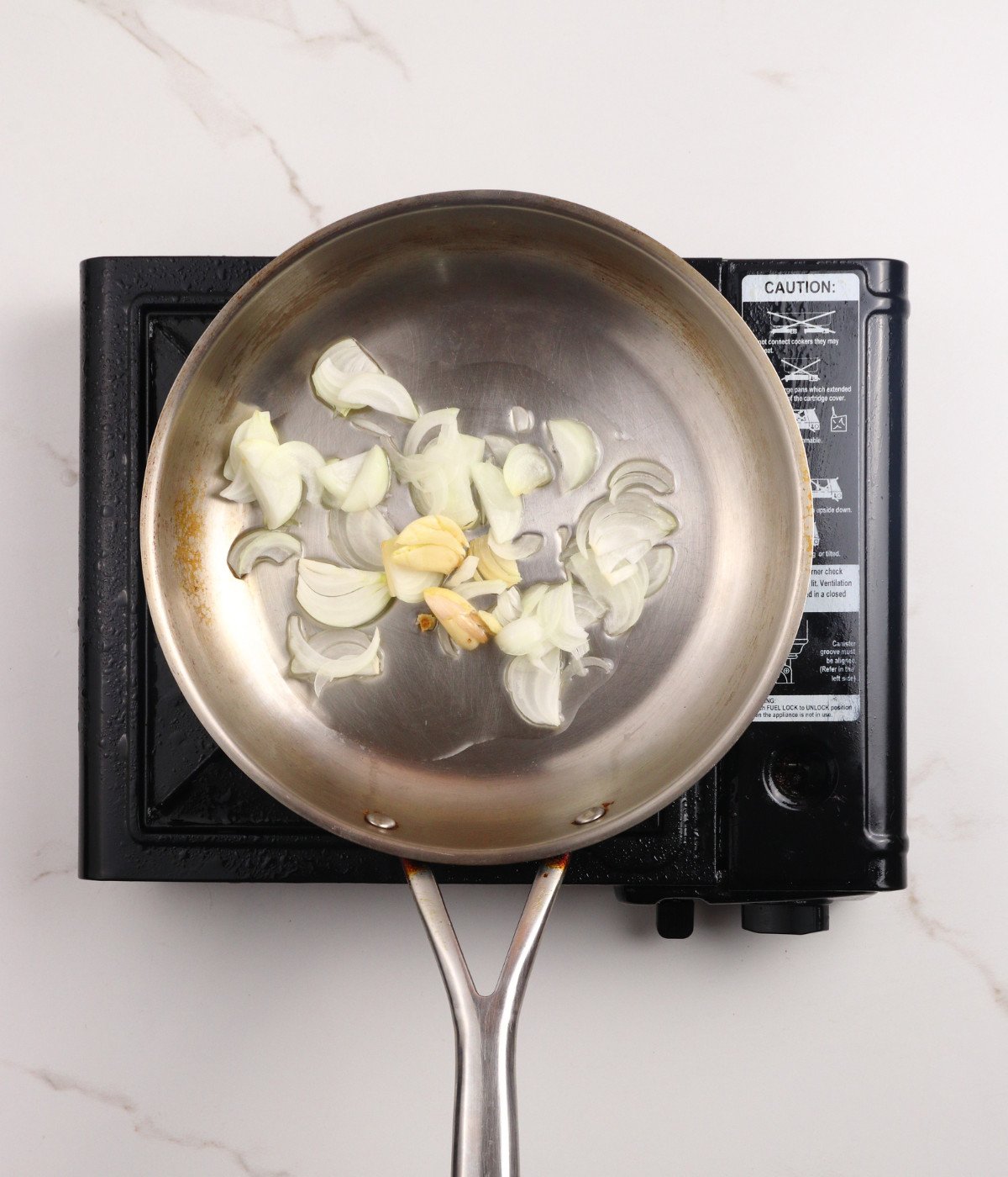Oil, onions, garlic cooking in a silver pan.