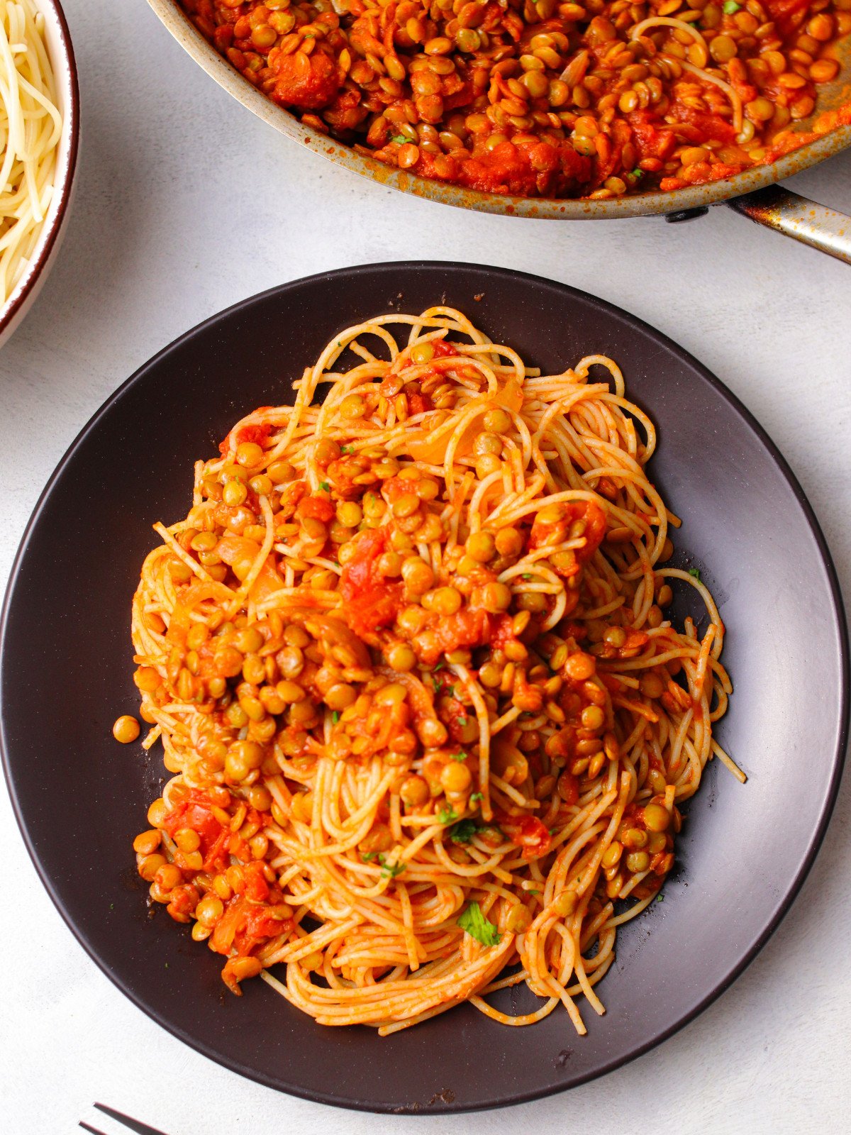 Spaghetti and lentil bolognese in a black plate.