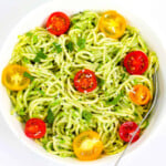 Spaghetti in avo sauce served with red, yellow baby tomatoes and fresh herbs in a white bowl.