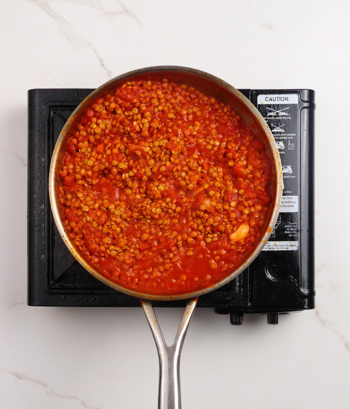 Tomatoes, onions, seasoning and green lentils cooking and stirred in a silver pan.