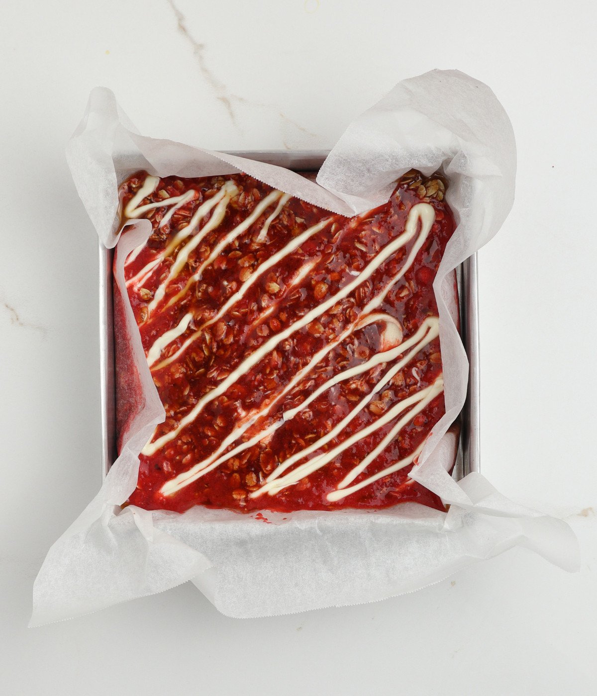 Oat mixture with crushed strawberries and white chocolate in a lined square silver tin.