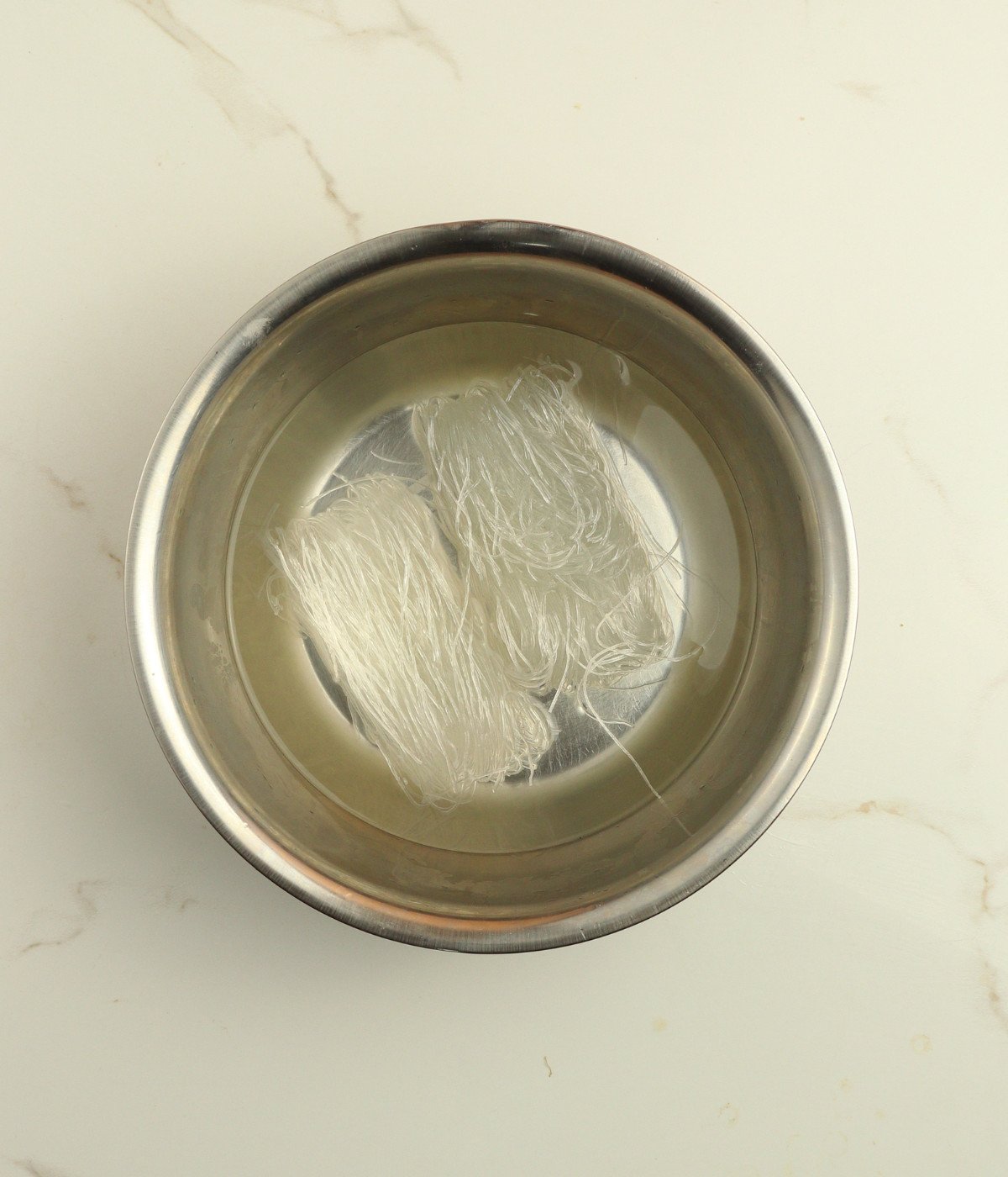 Noodles in warm water in a silver bowl.