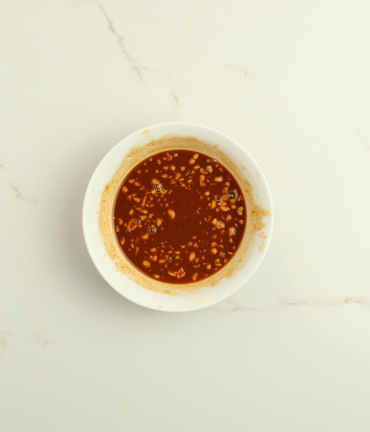 Peanut butter, soy sauce, lime juice and peanuts mixed in a white bowl.