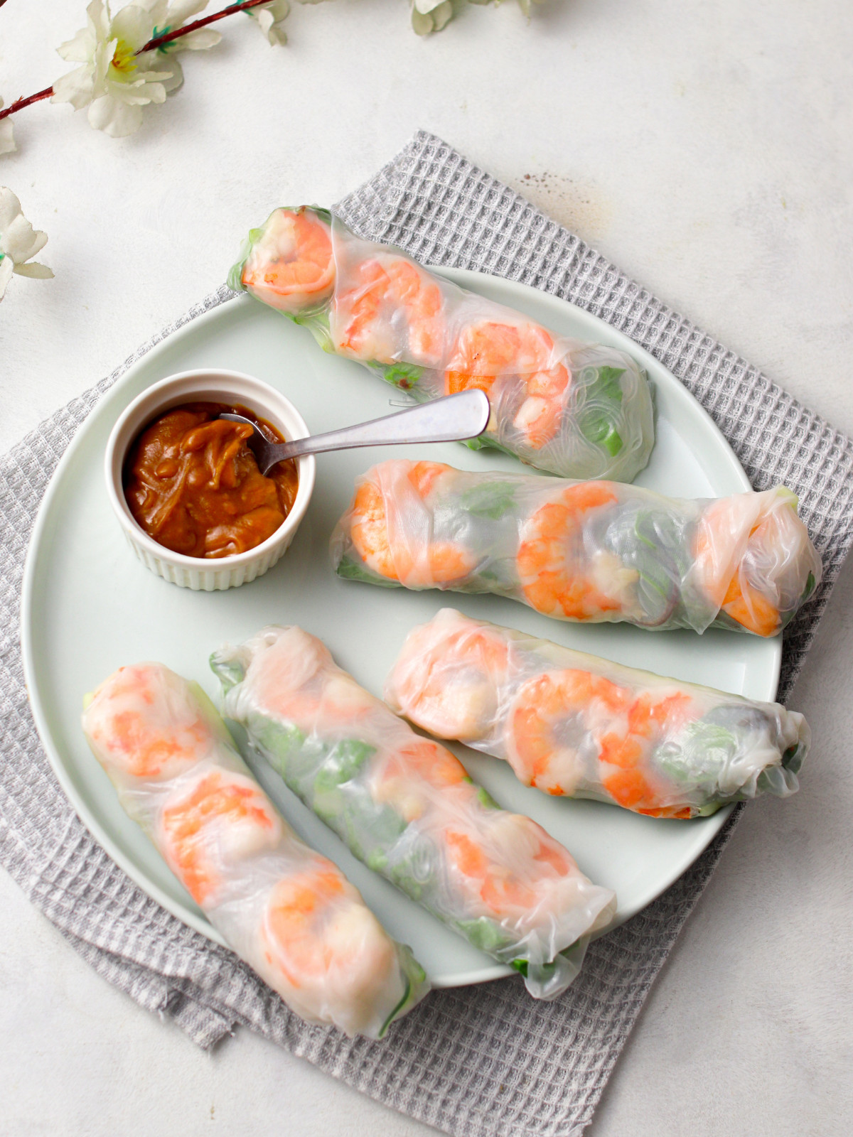 Shrimp summer rolls on a green plate with peanut sauce.