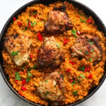Tomato bulgur wheat and chicken in a black pan with red chilies and fresh herbs.