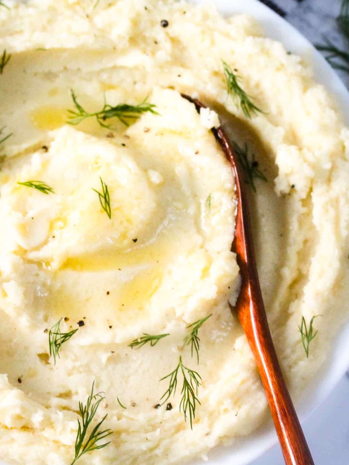 Creamy mashed potato in a white plate topped with butter and herbs.