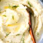 Mashed potatoes with belted butter and herbs on top in a white plate with a wooden spoon.