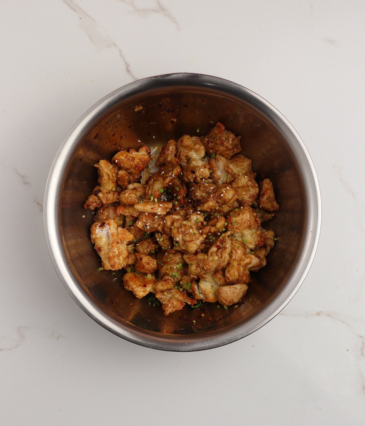 Baked chicken pieces tossed in orange chicken sauce in a silver bowl.