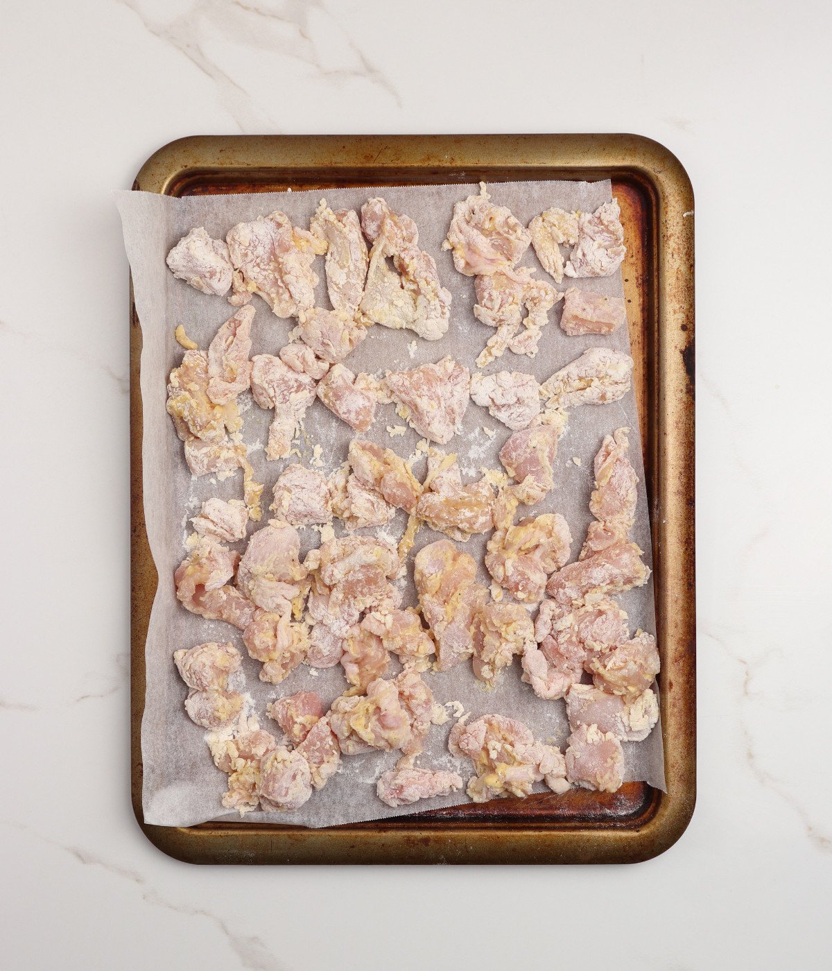 Chicken pieces coated in egg and flour mixture on a lined baking tray.