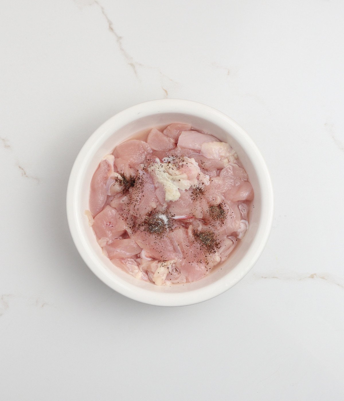 Chicken pieces, salt to taste, black pepper to taste and cornstarch in a white bowl.