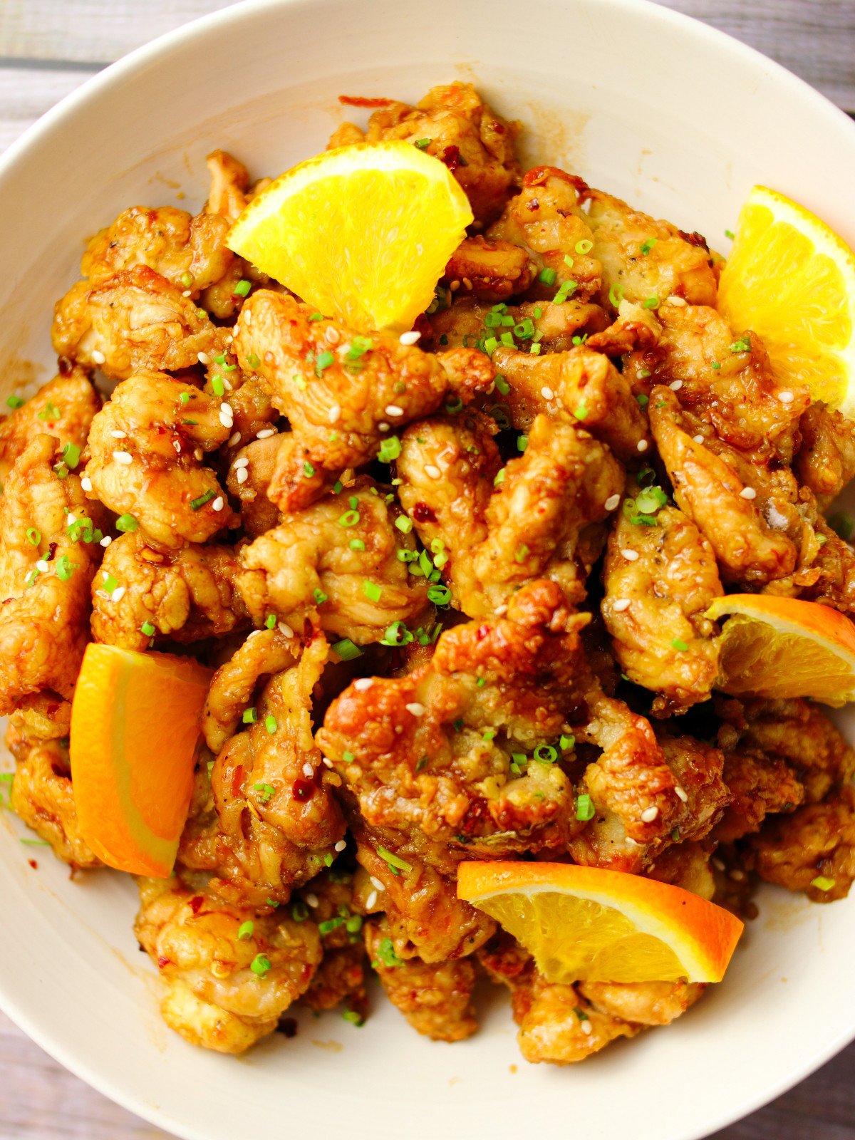 Orange chicken in a cream bowl with orange slices.