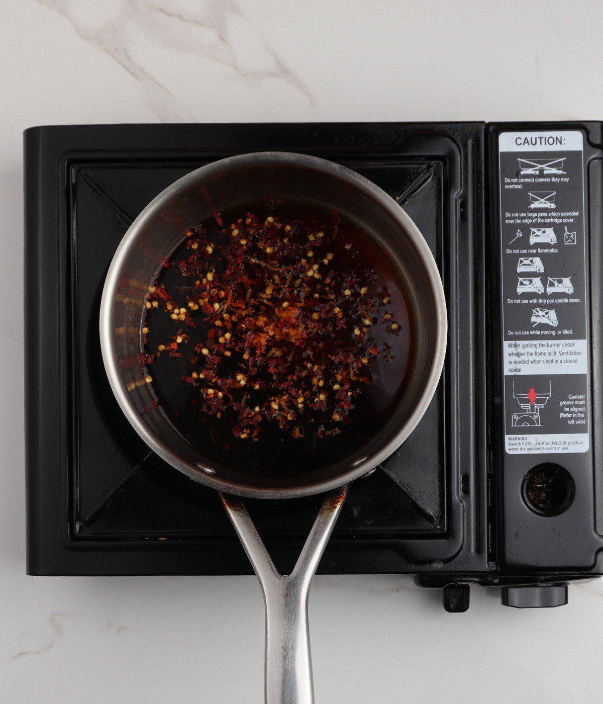 Soy sauce, orange chicken and chilli flake in a pot on a stove.