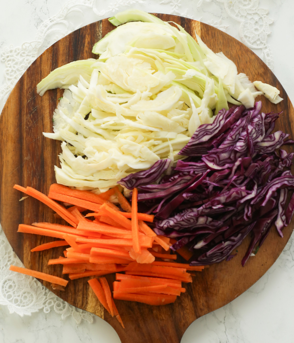 Chopped white cabbage, re cabbage and carrots on a brown board.