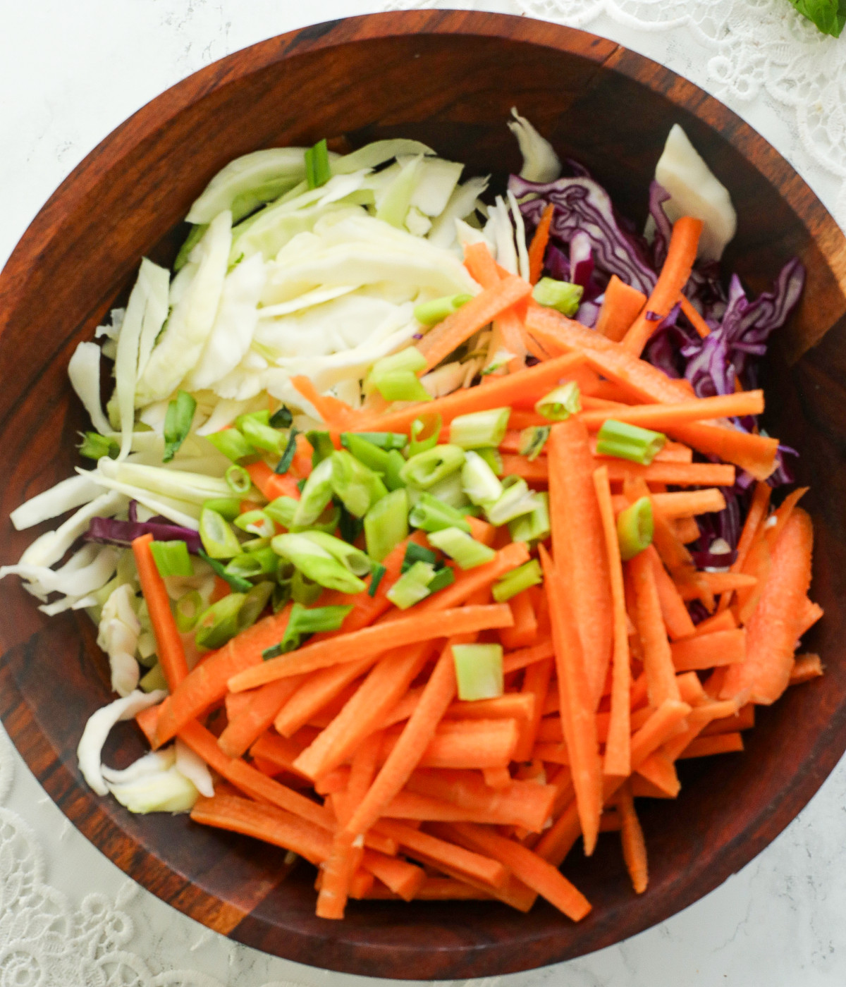 Chopped white cabbage, red cabbage, scallions and carrots in a brown board.
