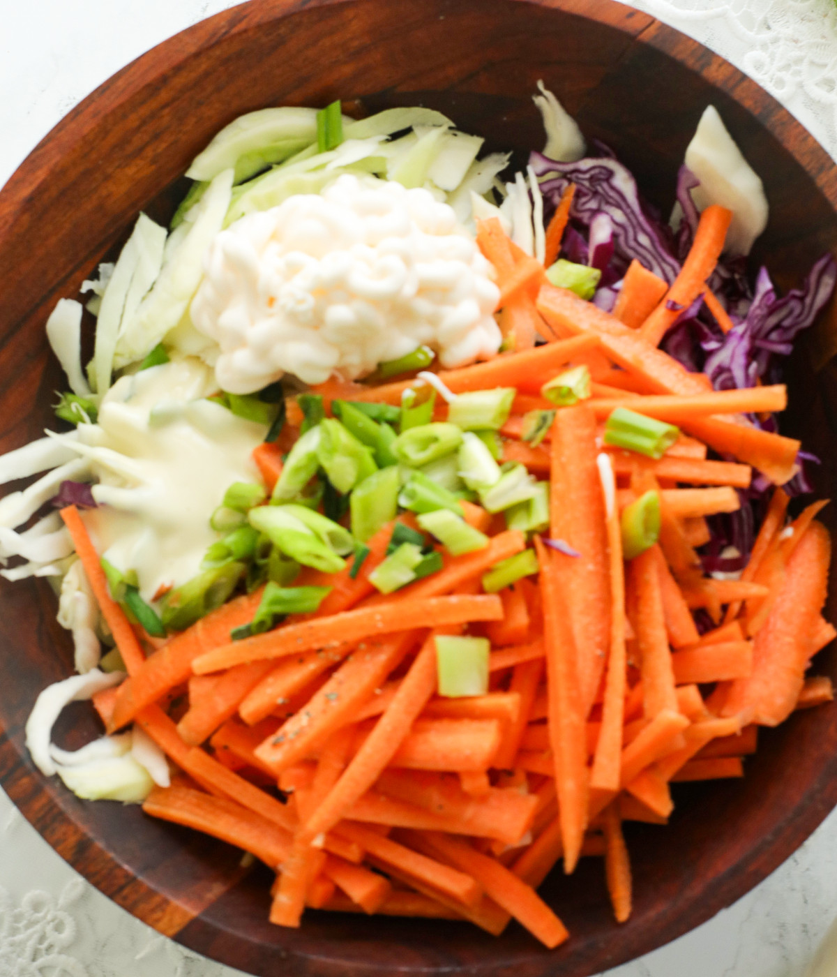 Chopped white cabbage, red cabbage, scallions, mayonnaise, salad cream and carrots in a brown bowl.