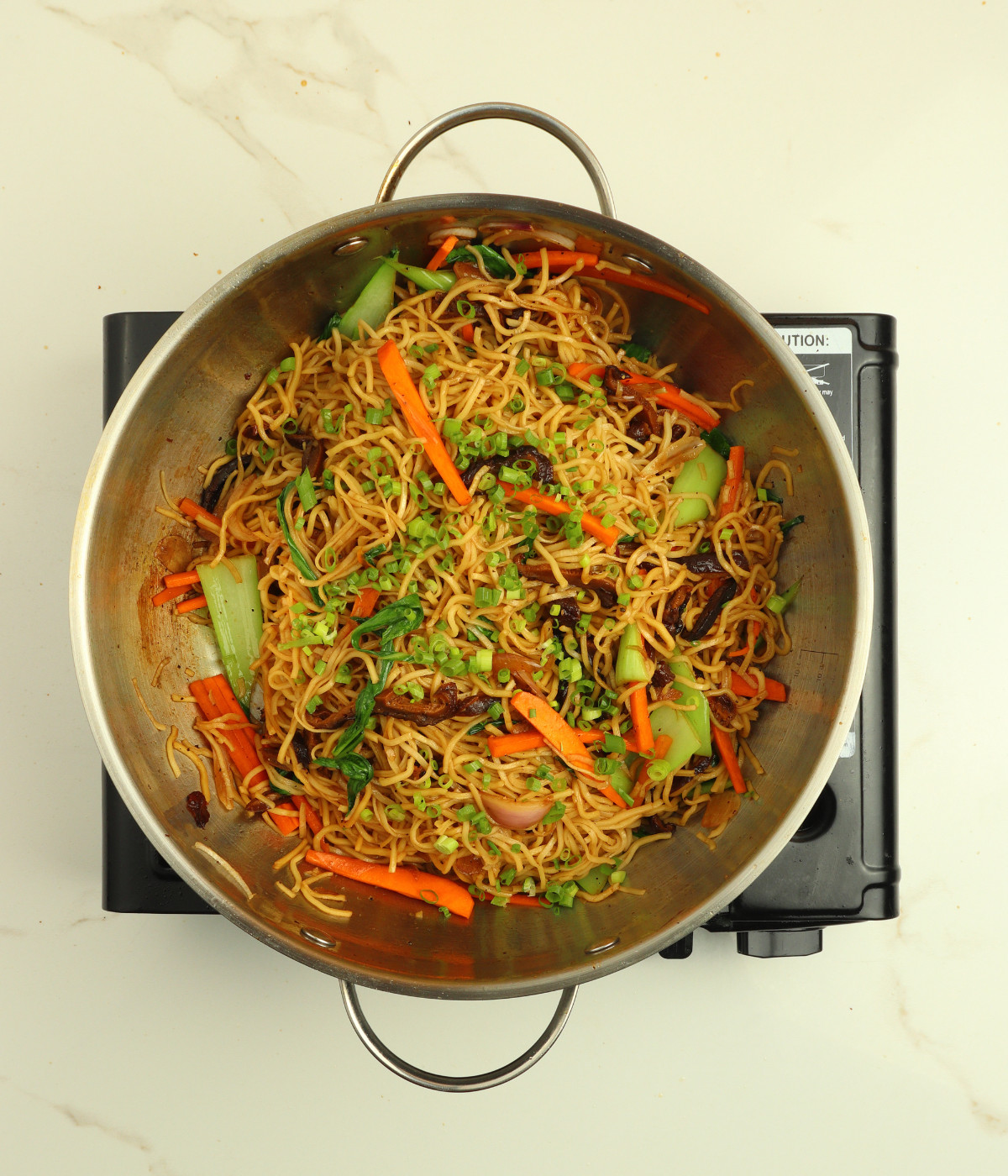 Mushroom, carrots, chow mein, pak choi and soy sauce tossed in a silver wok.