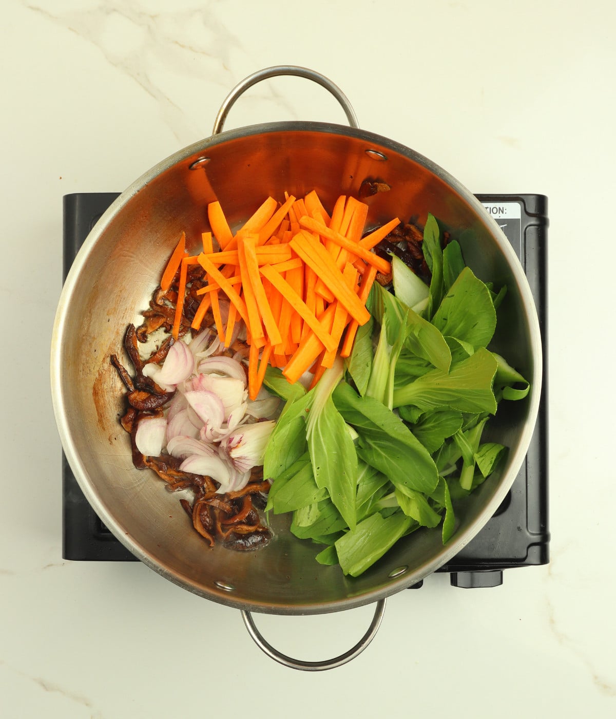 Mushroom, carrots, onions, pak choi and oil in a silver wok.