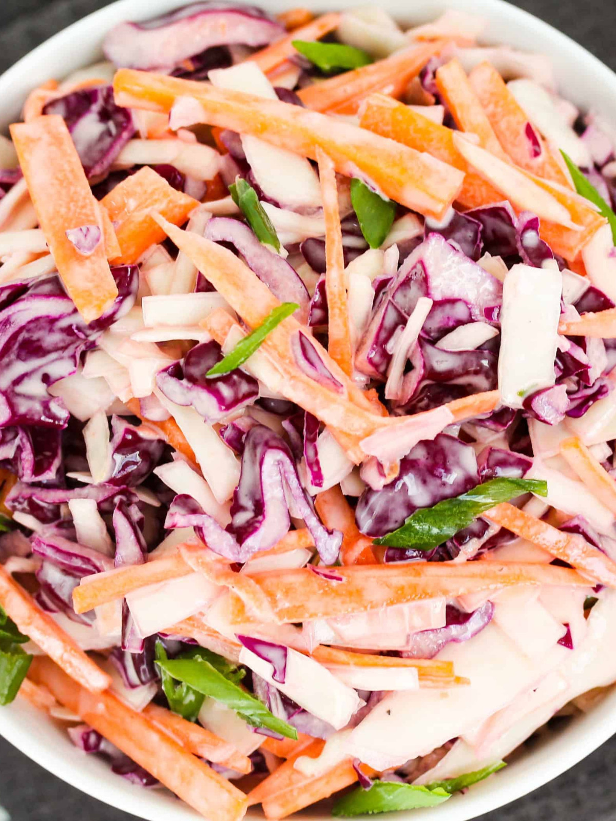 Red and white cabbage, carrots, green onions and mayo mixed in a white bowl.