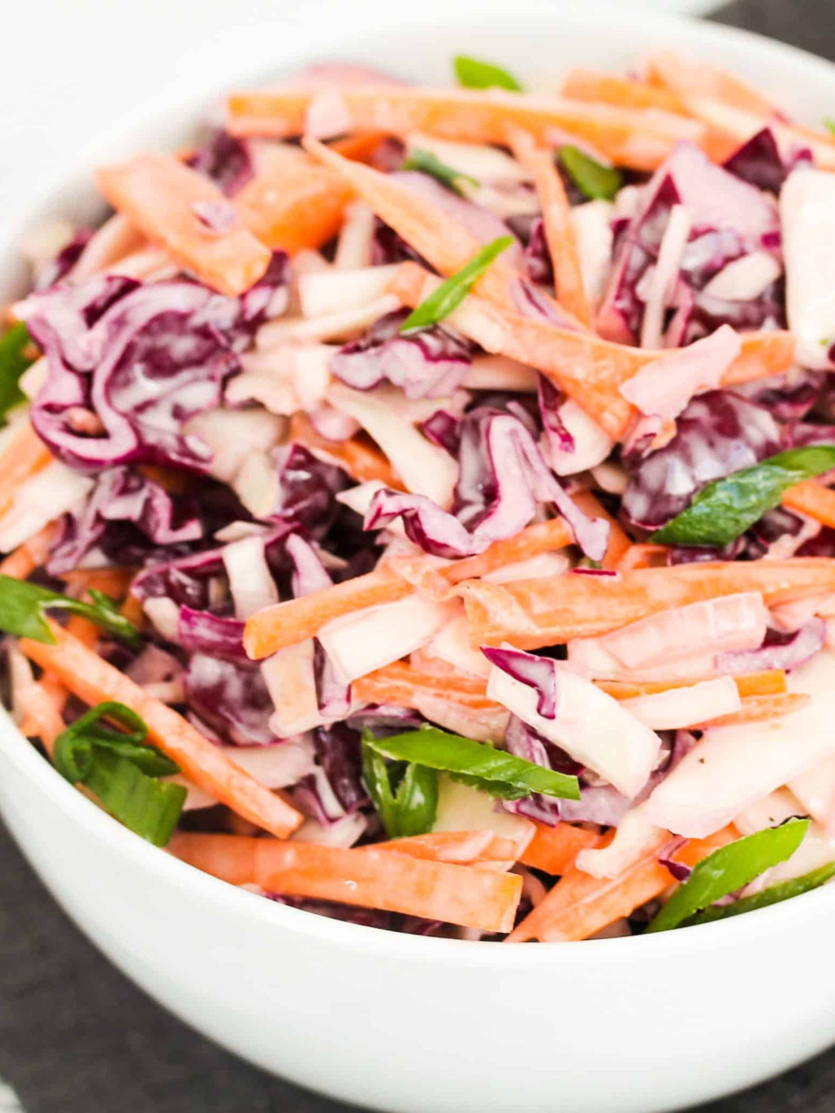 Red cabbage, white cabbage, carrots, green onions and mayo mixed in a white bowl.
