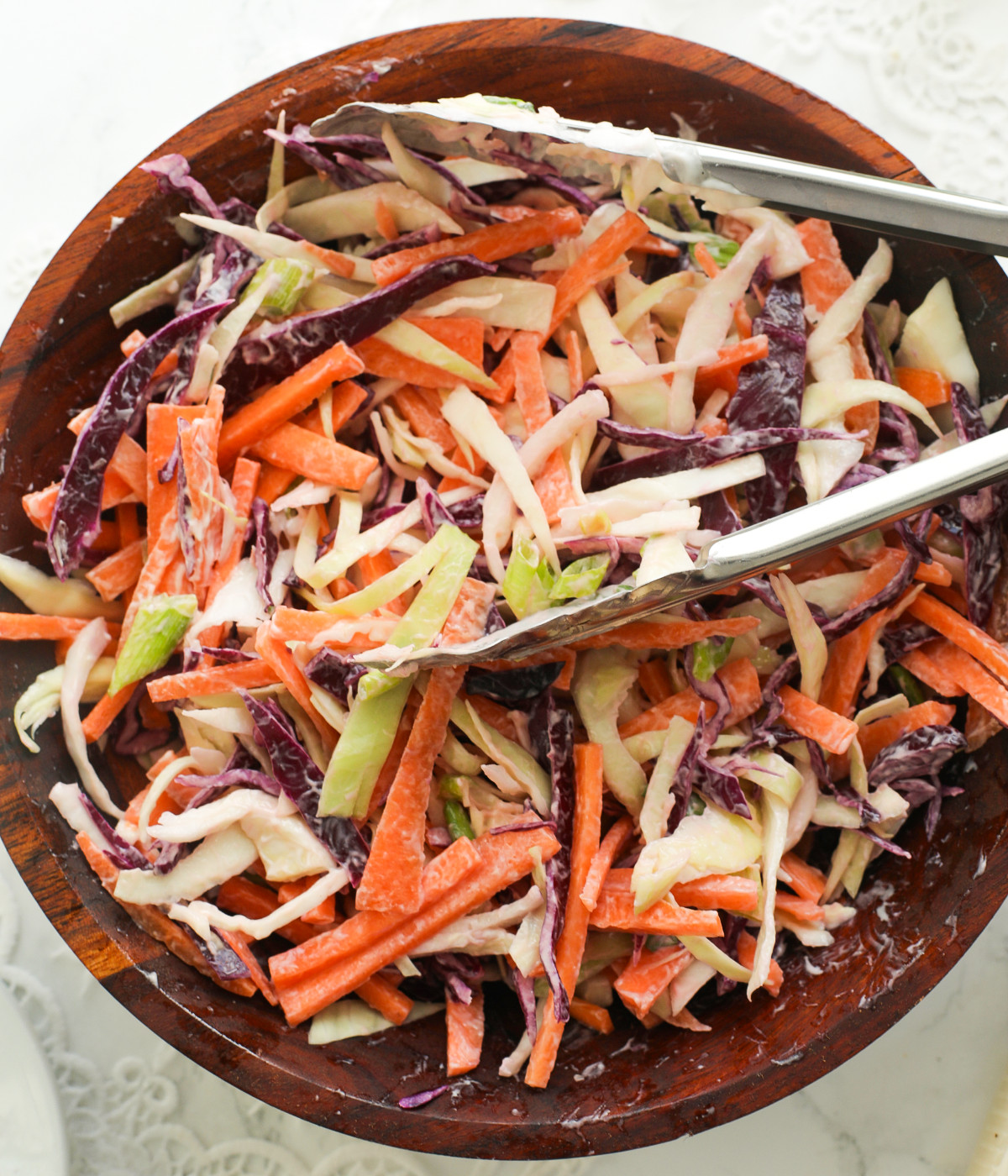 Red coleslaw in a wooden bowl with silver tongs.