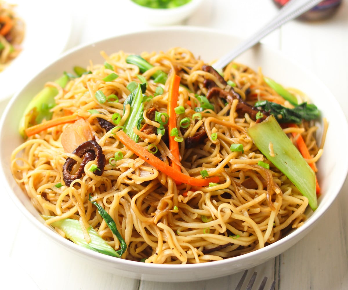 Chinese-style vegetable noodles in a white bowl with a silver fork.