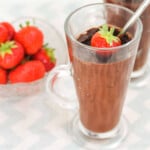 Chocolate avocado dessert in a tall cup with strawberries and s dessert spoon.