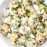 Chopped potatoes, boiled egg, mayo and red onions mixed in a white bowl
