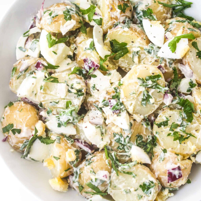 Chopped potatoes, boiled egg, mayo and red onions mixed in a white bowl