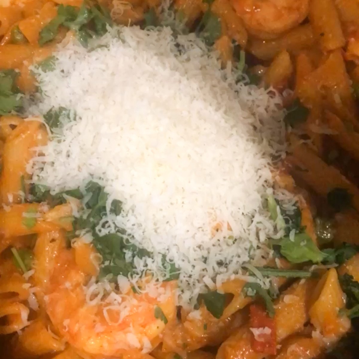 Cooked shrimp, penne pasta, peas, chopped sausages, grated parmesan, herbs and jambalay sauce stirred in a pot.
