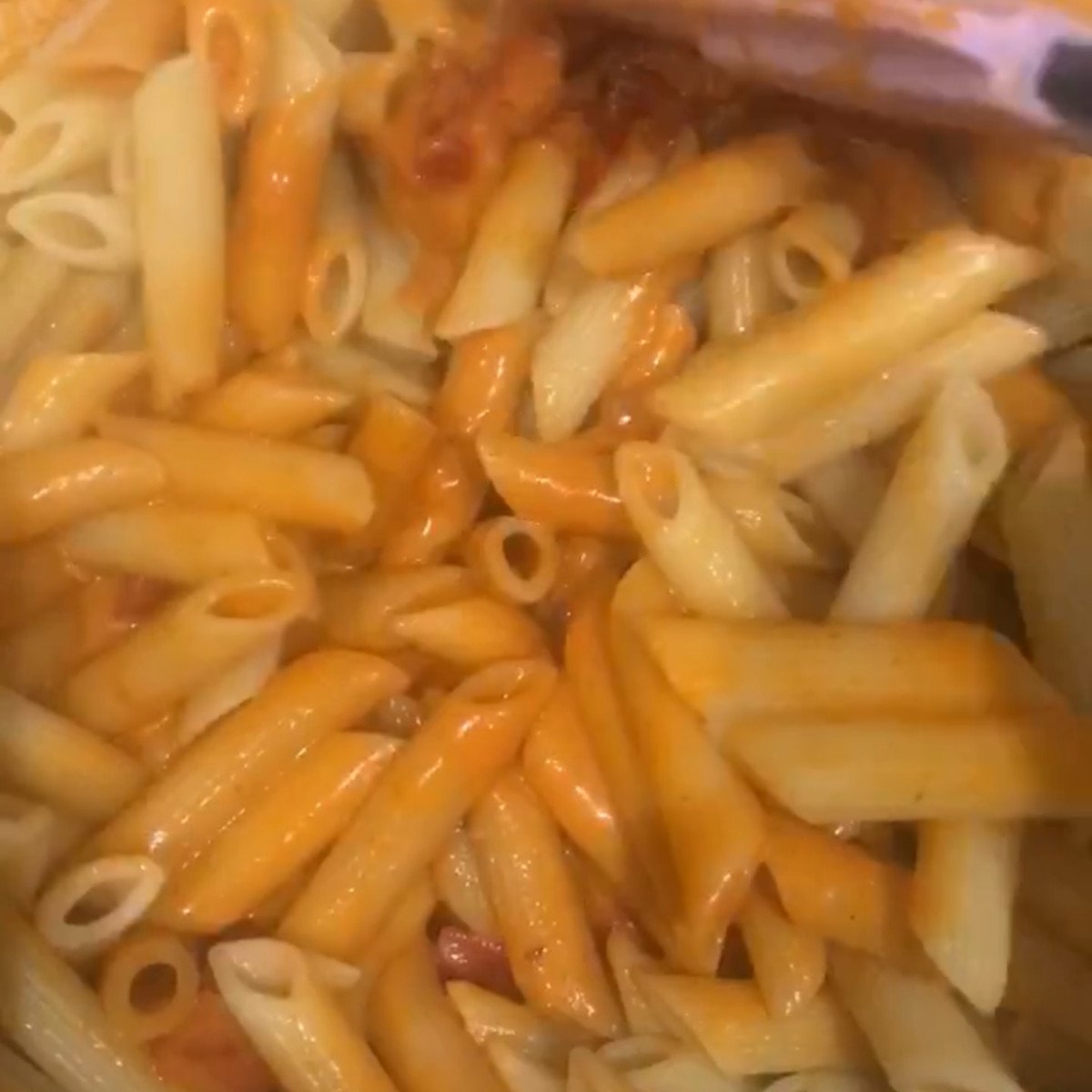 Penne pasta and jambalay sauce stirred in a pot.