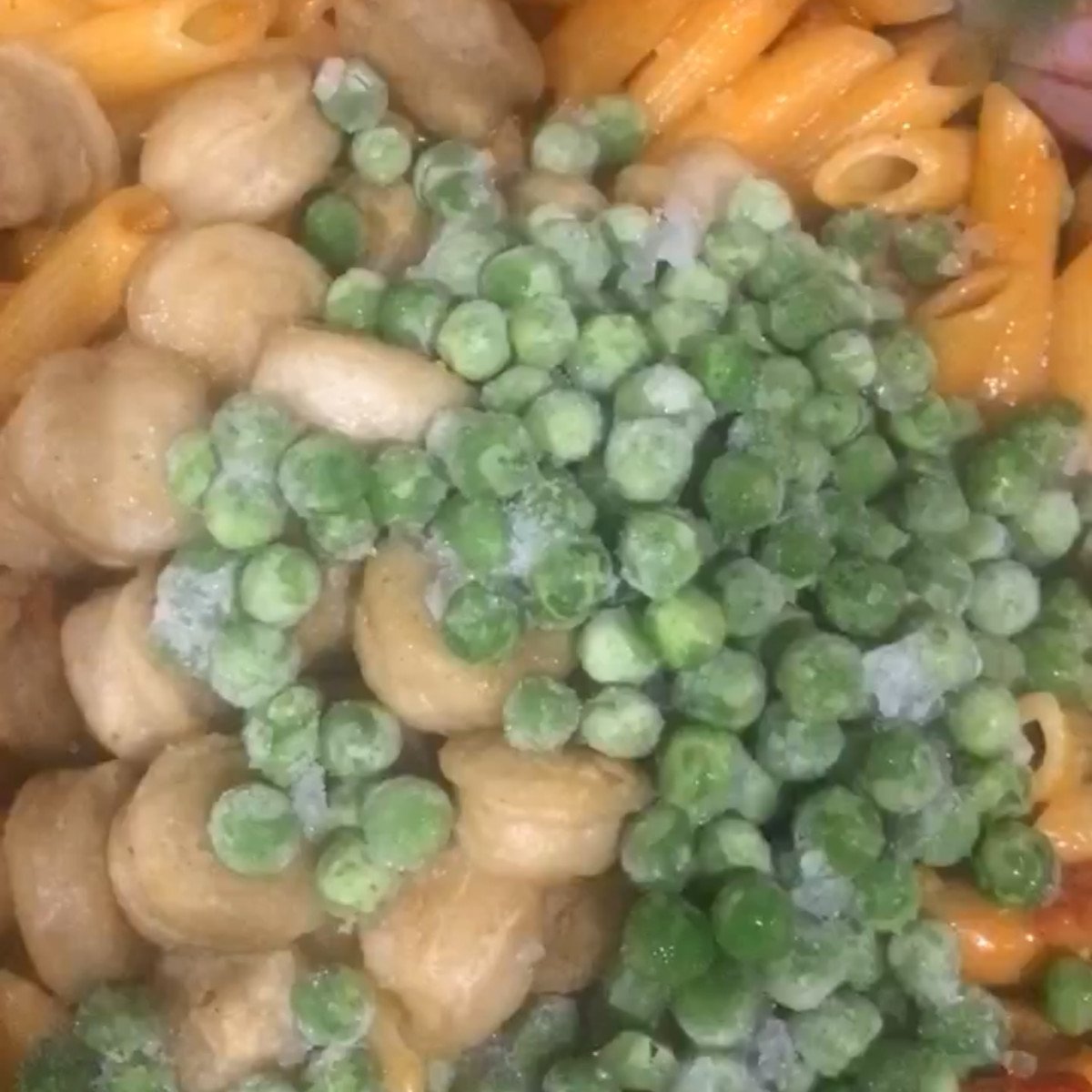 Penne pasta, peas, chopped sausages and jambalay sauce stirred in a pot.