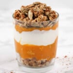 Pumpkin, yogurt, pumpkin seeds and granola in a glass cup.