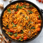 Tomatoes and creamy mushroom, spinach pasta in a black pan.