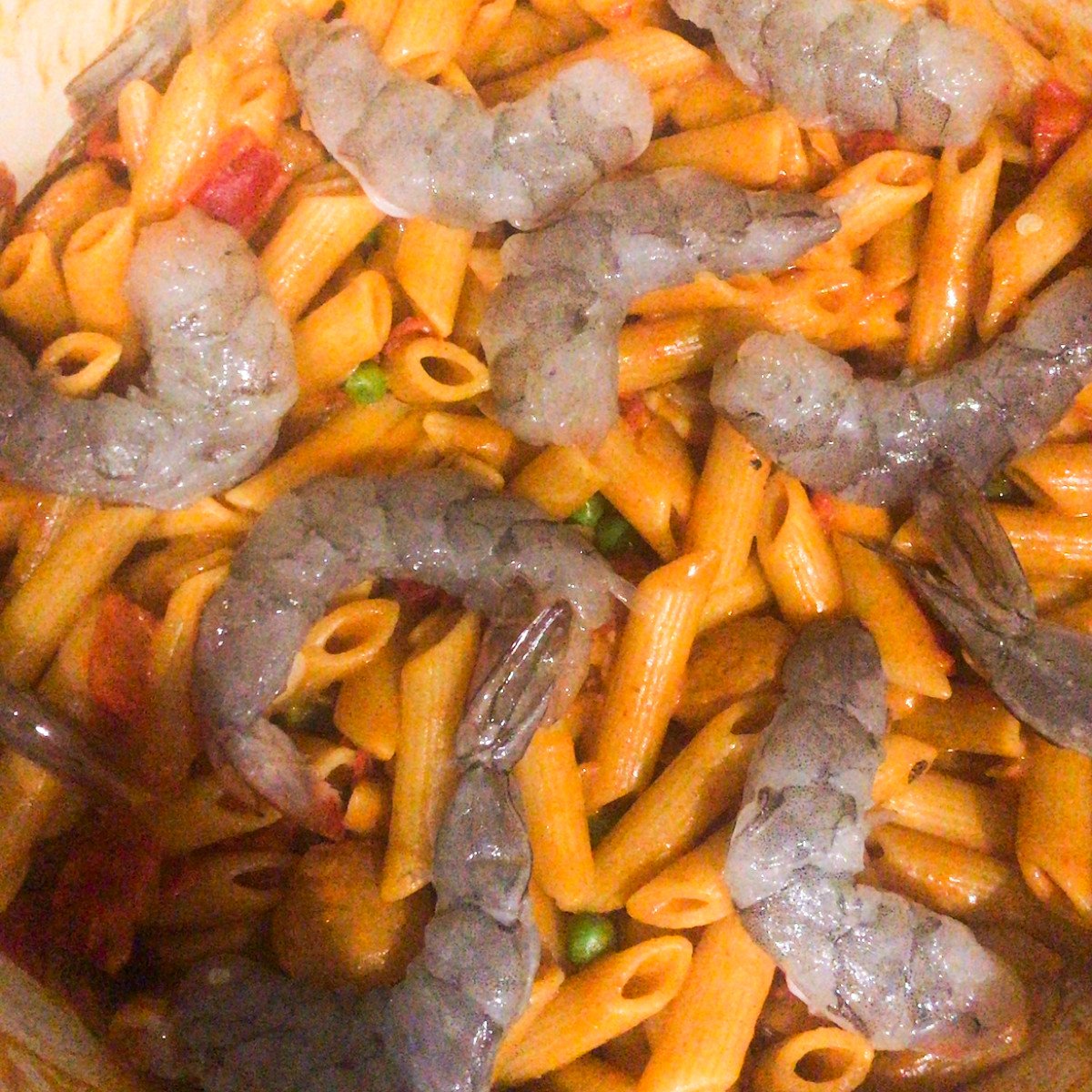 Uncooked shrimp, penne pasta, peas, chopped sausages and jambalay sauce stirred in a pot.