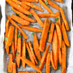 Baked sweet potato chips on an oven tray topped with parsley and salt.