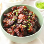 Beef teriyaki in a green bowl topped with sesame seeds and green onions.