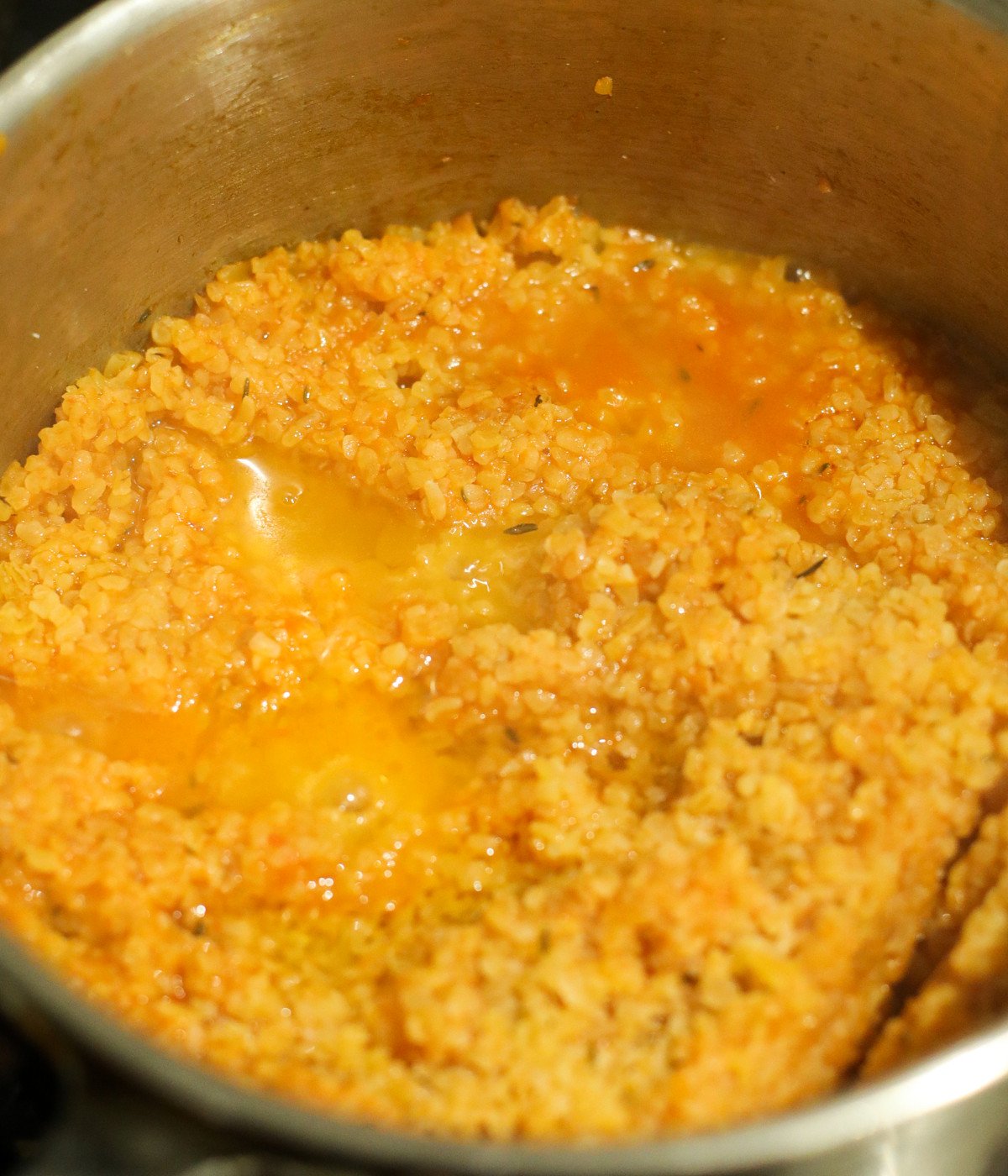 Blended tomato mixture and bulgur wheat cooked in a silver pot.