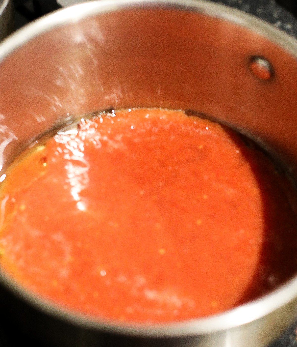 Blended tomato mixture and vegetable oil in a silver pot.
