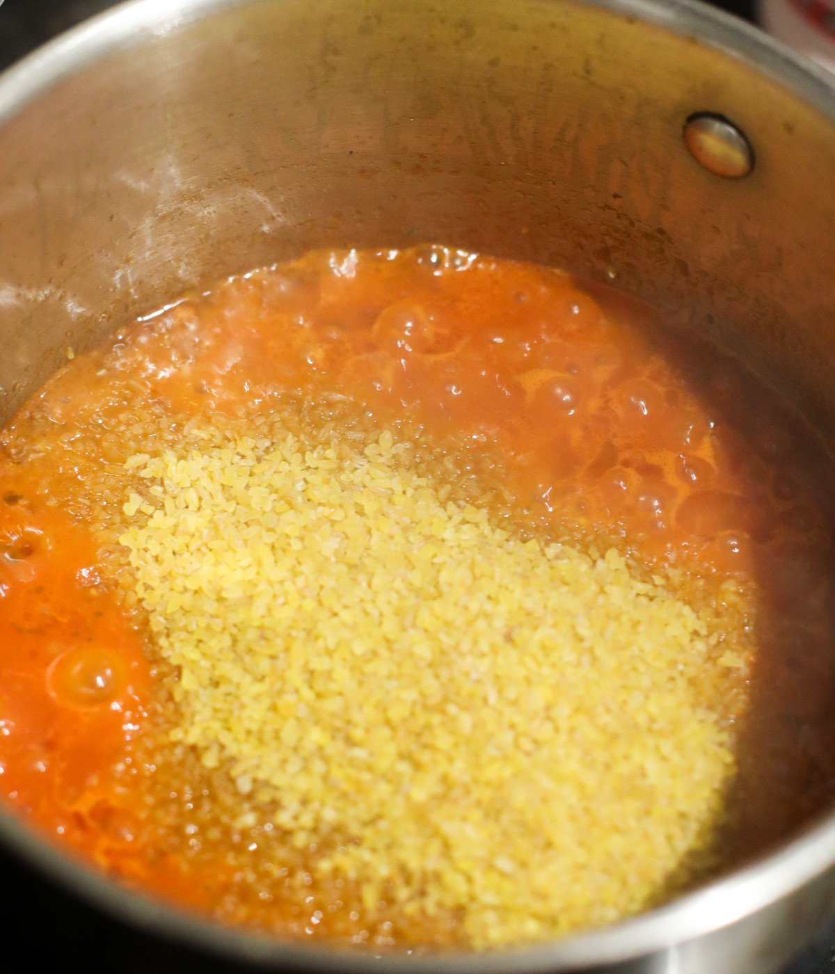 Blended tomato mixture, seasoning and bulgur wheat in a silver pot.