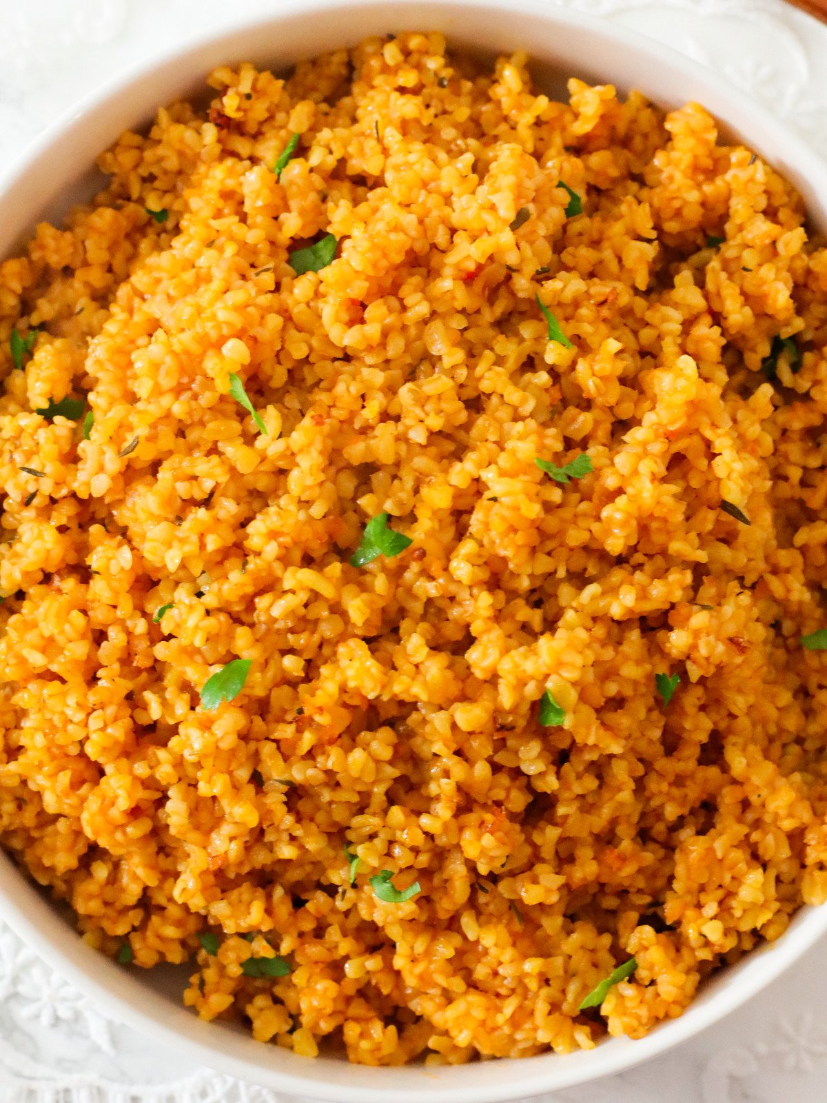 Bulgur jollof in a white bowl with fresh herbs.