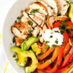 Chicken, avocado slices, capsicum peppers, and sour cream in a white bowl.