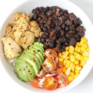 Chicken, black beans, avocado, tomato, corn in a white bowl.