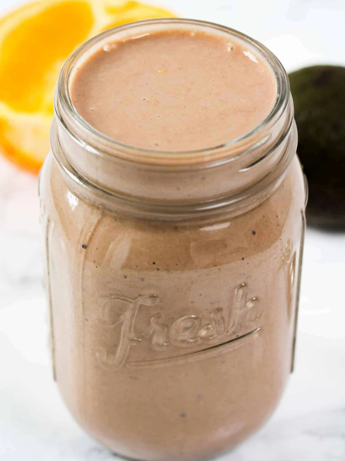 Chocolate smoothie in a jar with an orange on the table.