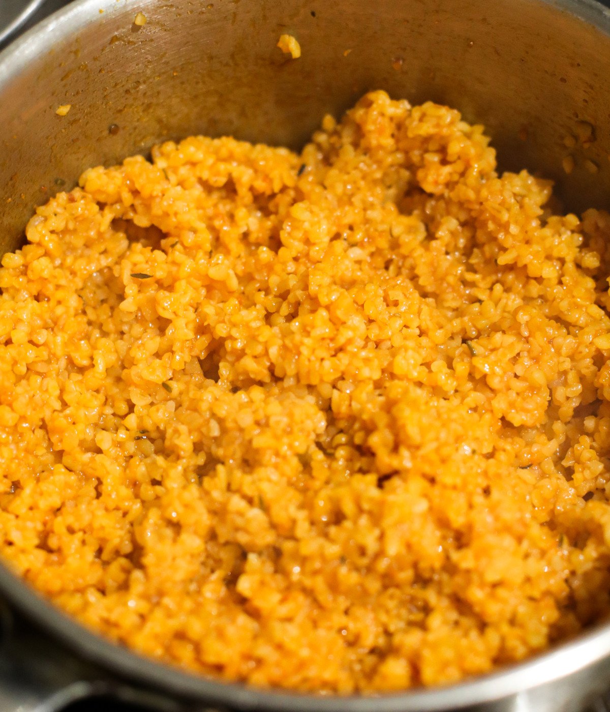 Cooked bulgur wheat, tomato sauce and seasoning a silver pot.
