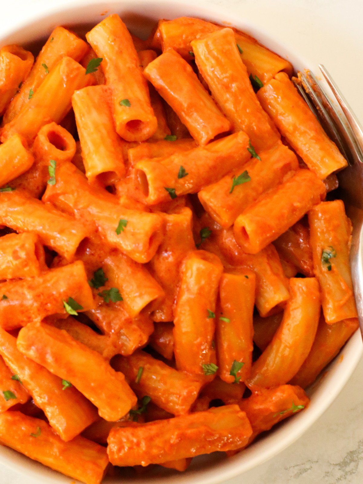 Creamy tomato rigatoni in a white plate garnished with parsley.