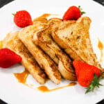 Egg toast with syrup and strawberries on a white plate.