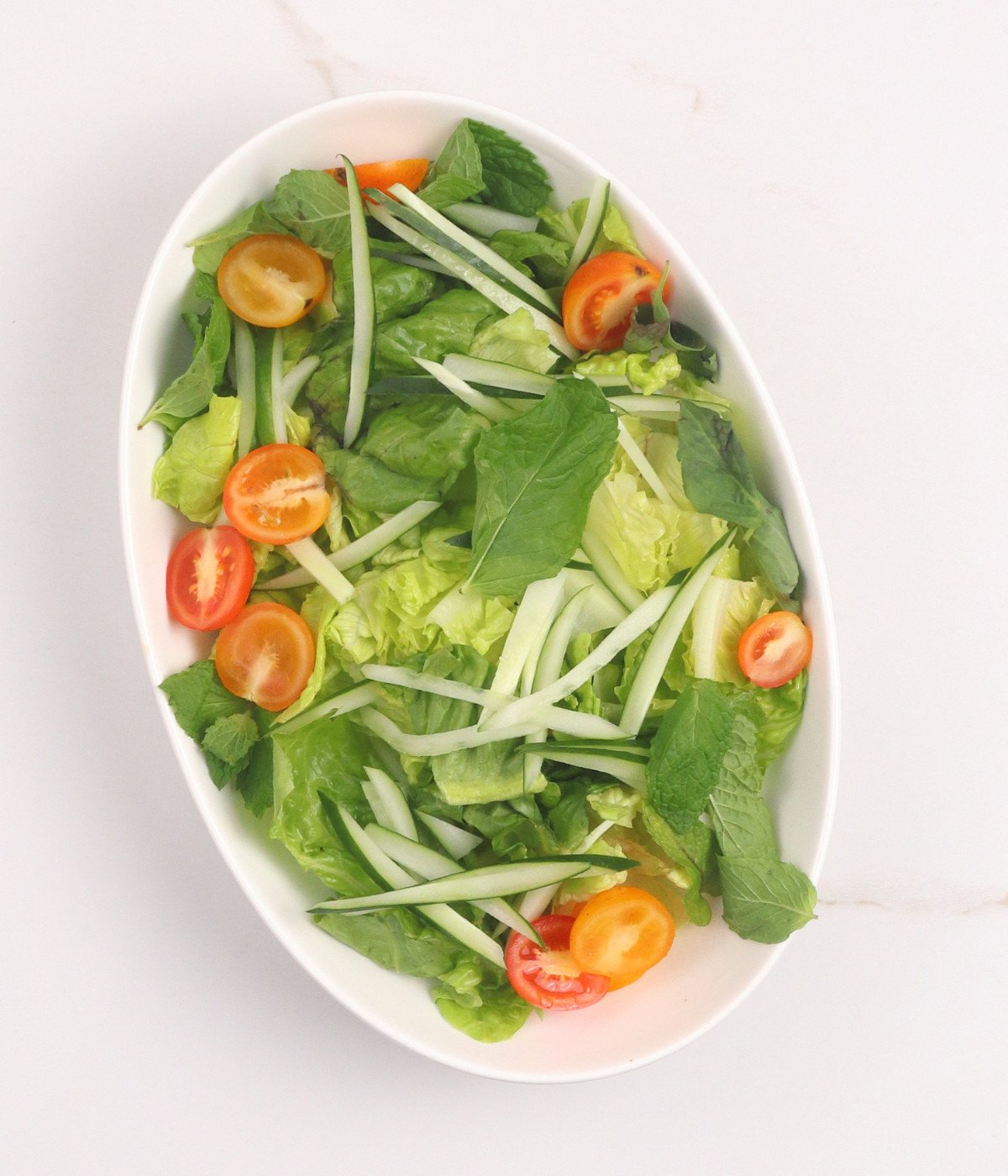 Lettuce, cucumber, and tomatoes in a white oval bowl.
