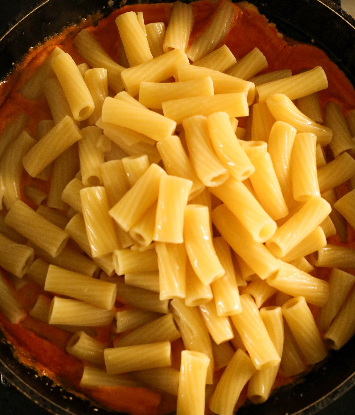 Rigatoni and creamy tomato sauce in a black pan.